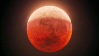 A red-coloured full Moon in partial lunar eclipse against a dark night sky