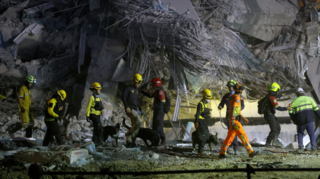 Rescuers in technical gear walk along the remains of a collapsed high-rise building under construction in Bangkok