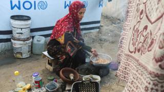 Displaced Palestinian woman Hanan Abu Taibah cooks food on a fire outside her tent in Khan Younis, southern Gaza (18 December 2025)