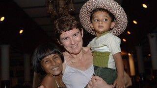 Sian Hughes, with short brown hair, is looking at the camera, with two small Sri Lankan children on either side    