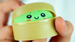 Close up of a hand holding a bright green dumpling toy inside a plastic steamer container.