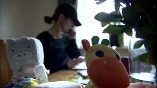 A woman wearing a dark baseball cap and t-shirt sits in front of a window with children's toys in the foreground