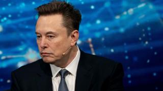 Close up of Elon Musk wearing a suit against a blue background