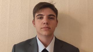 Yaroslav poses for the picture. he is in a shirt, tie and blazer. It is a close up of his head and shoulders. He has brown hair 