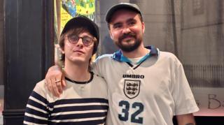 George Wright, wearing a Euro 96 England shirt with 32 on the front, puts his arm around his brother, Laurie, wearing a stripey long-sleeve t-shirt while standing outside a pub in central London. 
