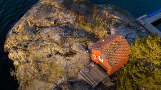 A small red hut with a jetty attached sits on an island.