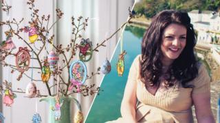 A picture of Amy Swann, with long dark hair and wearing a yellow summer dress, sitting on a ledge with the sea behind her, alongside an image of her Easter tree, which has twigs and branches coming out of a jug, with colourful decorations and baubles hanging from them.