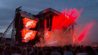 Red light emanates from BBC Radio 1's main stage at night as a crowd gathers in front.