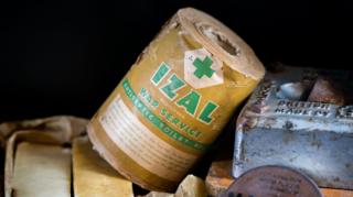 An old-looking roll of Izal toilet paper, the type that would have been used by the military in WW1. The paper cover around the roll says "Izal, Registered, War Service, Antiseptic Toilet Roll".