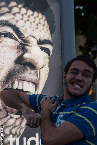 A man holds his arm in front of an advertising placard showing Suarez flashing his teeth at Copacabana beach in Rio de Janeiro