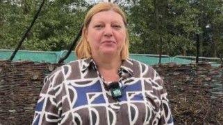 Jacqueline Mooney, with shoulder-length hair parted in the middle and wearing a geometric brown, blue and black shirt, stands in the centre of the charred roundhouse remains