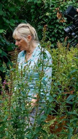 Woman with blonde hair in her garden with large green plants around her.