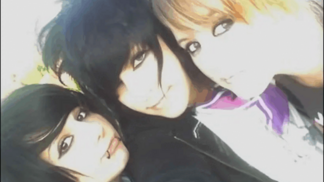 Three people taking a picture of themselves. A girl on the left has black hair in a swoop fringe, she has thick black eyeliner and snake bite piecings. The person in the middle has short black hair and a long fringe, also wearing black eyeliner. The person on the left has short blonde hair and thick black eyeliner. 