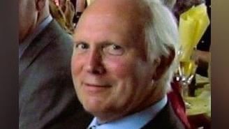Leonard Fuller in a suit and tie smiling at the camera. He has grey hair and appears to be at an event.