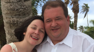 Philip Morris, wearing a white shirt, with his wife Dana. The couple are smiling and have palm trees behind them