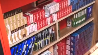 Cigarette boxes and tobacco pouches stashed under a shop counter, stored on wooden shelves.