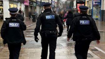 Three police officers seen from behind as the walk through Chatham town centre.