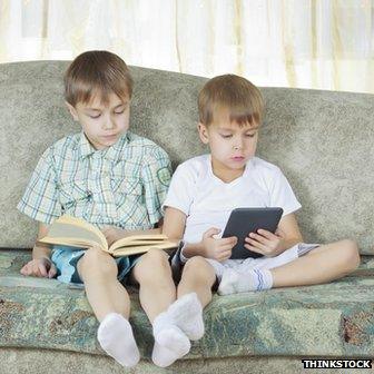 Two boys, one reading a book, one an e-reader