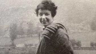 A vintage black and white photograph of Nan Green, smiling at the camera, with a large coiled rope over he shoulder