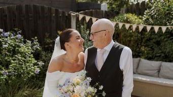 A woman in a wedding dress holding flowers and hugging a man in a suit in a garden