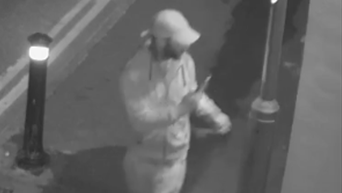 A black and white CCTV image of a man in a tracksuit and a hot holding a phone