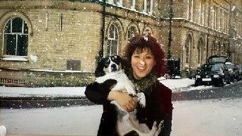 Chantana Parkinson smiles while holding her dog. She is standing outside her shop and it is snowing.