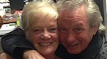A close-up image of an elderly couple, smiling, with their arms around one another. On the left, Sheila Jackson has short blonde hair and Eric Greener has thick grey hair.