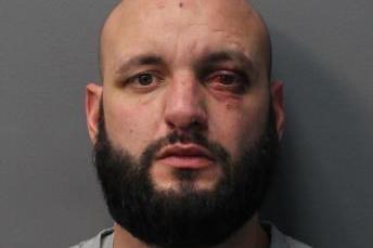 Ross Hamilton mugshot. He is a bald white man with a beard and looks towards the camera. He has visible injuries to one eye and the side of his head