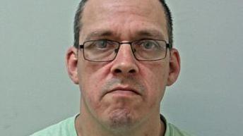 Custody image of Gary Wanless wearing black glasses and bright green t-shirt. 