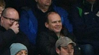 A crowd sit in a stadium watching a game.