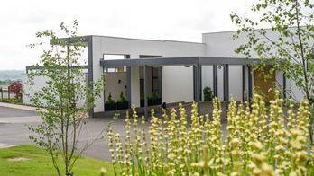 Modern white and grey crematorium building with grass and flowers in the foreground