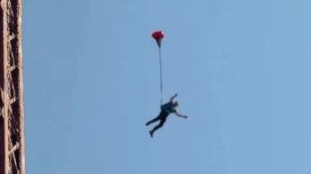 A man jumping from Blackpol Tower. He is seen suspended in mid-air with a red balloon attached to him. Blue sky and the edge of the tower can be seen in the background.