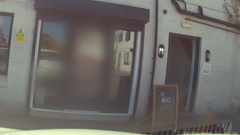 A still from a dashboard camera showing a doorway in a brick building covered by white paintwork. An A-board with 'The Hart Space' written in chalk is visible outside.