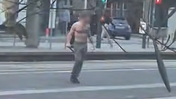A bare chested man carrying what appears to be a large knife on a street