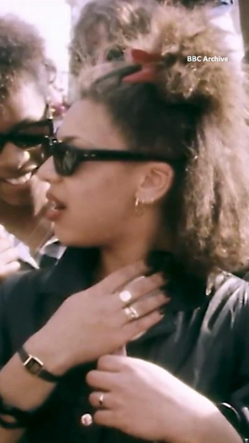 A woman with sunglasses, frizzy hair and a dark jacket