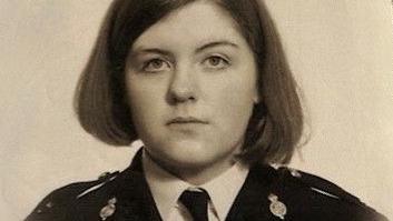 The photo is vintage and sepia toned. It's of a young woman with her dark hair cut into a bob. Her expression is serious as she looks at the camera, and she's wearing a police uniform.