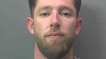 Matthew Fox, a bearded man, stares at the camera in a police custody photo