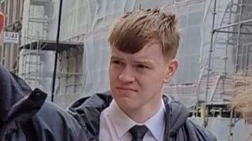 A red-headed teenager wearing a shirt and tie outside a court