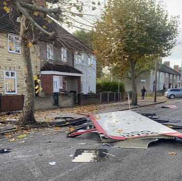 A view of the roof of the bus lying on the road in a tree-lined residential road. It is surrounded by associated debris