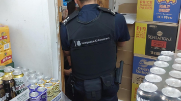 A male immigration enforcement officer in a black vest and blue polo shirt looking into a store cupboard