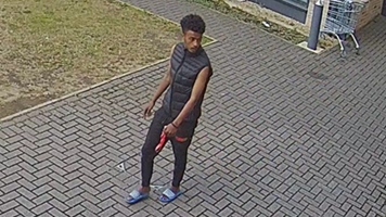 A man in a black vest, black trousers and blue sliders captured by CCTV in a building. He is looking away from the camera.