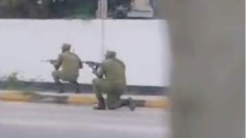 Two men in green police uniforms kneeling down pointing rifles down a street