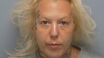 A mugshot of a woman with light blonde hair and face tattoos