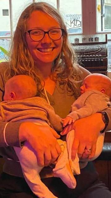 A blonde woman with glasses holding two babies.