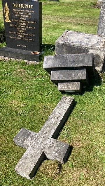 A cross-shape headstone lies face down in the grass