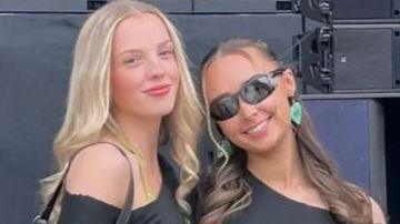 A woman with long blonde hair stands beside another with tied up dark hair both are smiling toward the camera