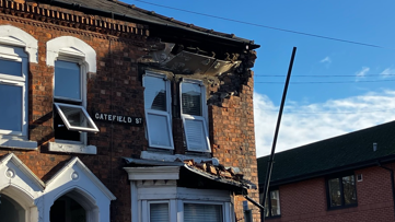 The corner of an early-20th Century terrace, where a large chunk of brickwork has fallen away around an upstairs window, some landing on top of the bay window below 