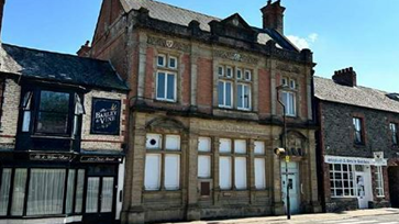 The former bank building on East Street in South Molton, Devon is pictured, with its period features and located next to other shops/ establishments, on a bright, sunny day, with blue skies overhead. 