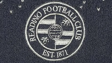 The image shows a close up of the Reading Football Club's badge on a grey woollen hat. The badge is grey and white. Instead of saying "READING FOOTBALL CLUB" the writing in the badge says "READINO FOOTRALL CLU8".
