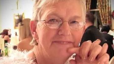 Wilma Porter, looking into the camera with her hands under her chin. She has short grey hair and is wearing glasses. 